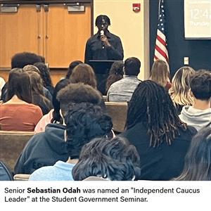 Senior Sebastian Odah stands in front of group of students speaking into a microphone