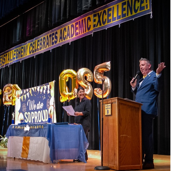   Principal stands at podium speaking into microphone to welcome crowd