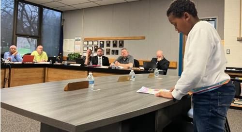Student from Logan stands up and shares updates with the board