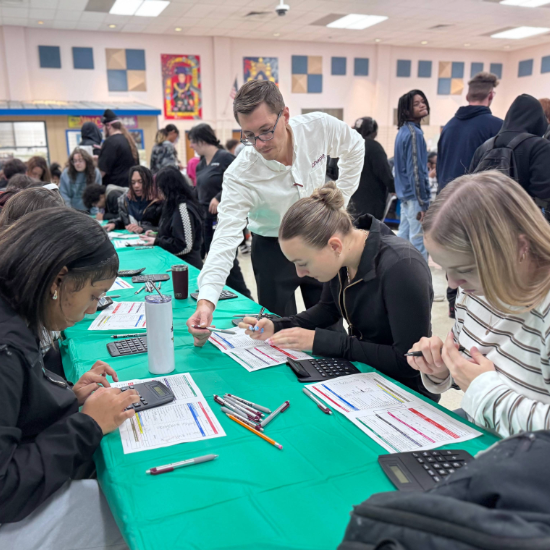  man helps students at table complete their budgeting exercise